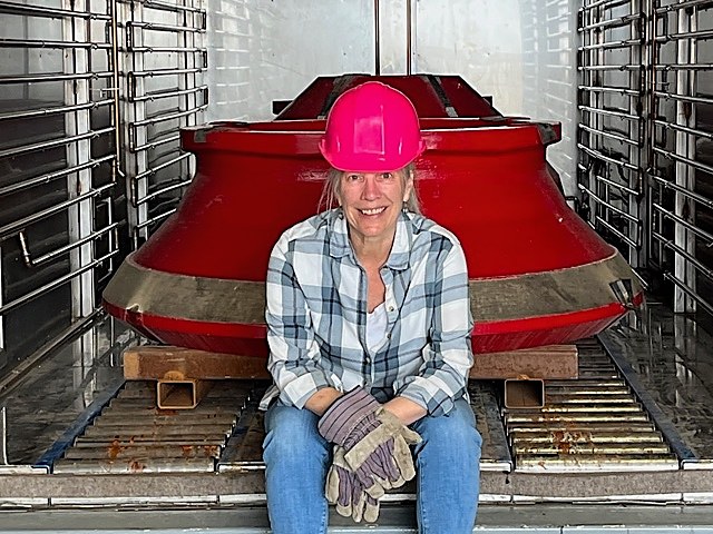 Linda Williams in a hard hat in front of a red crusher mantle inside a DCI chamber